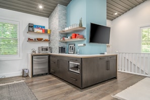 A modern kitchen with a built-in oven, microwave, and sink, featuring dark cabinetry and light blue walls. - Carriage House - Studio Condo minutes away from downtown Saugatuck! (Saugatuck)