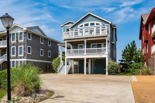 A multi-story residential building with a balcony on the second floor, a garage, and a driveway.