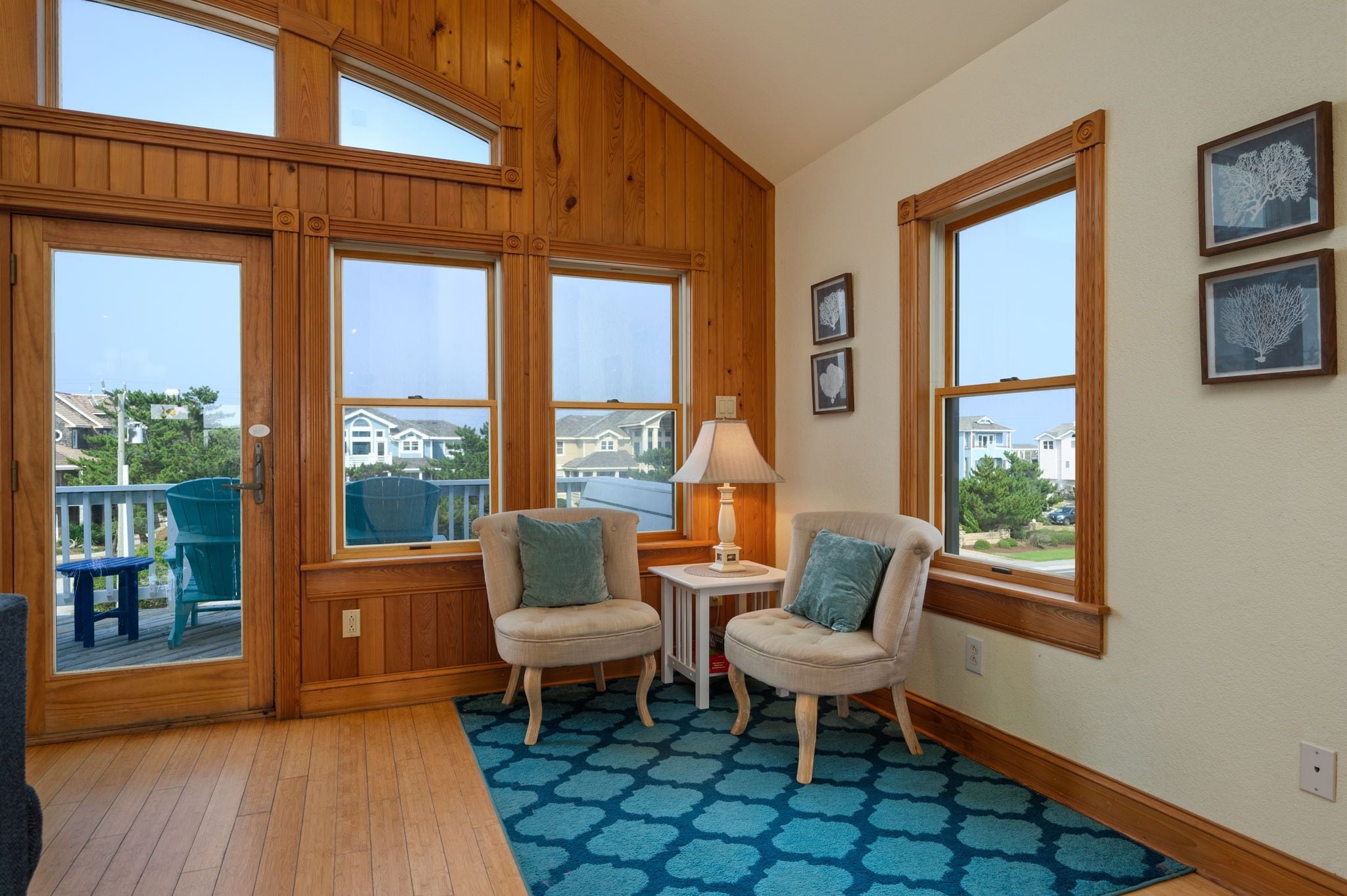 A room with wooden paneled walls, large windows, two chairs, a small table, and a blue patterned rug.