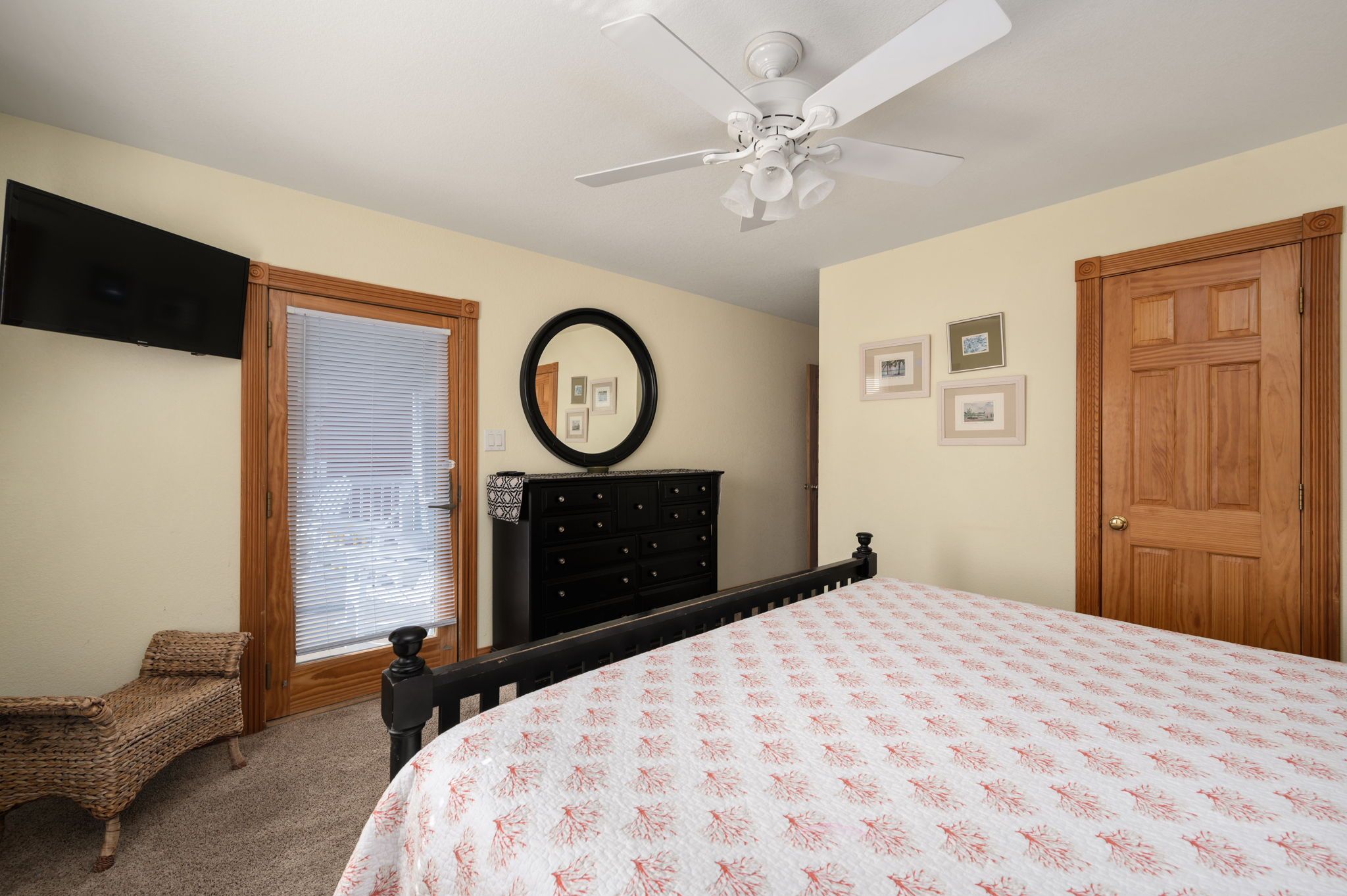 A bedroom with a bed, a dresser, a ceiling fan, a window with blinds, and a door.