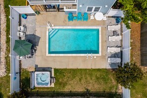 Vista aérea de um quintal com piscina retangular, cercada por cadeiras de descanso e uma banheira de hidromassagem.