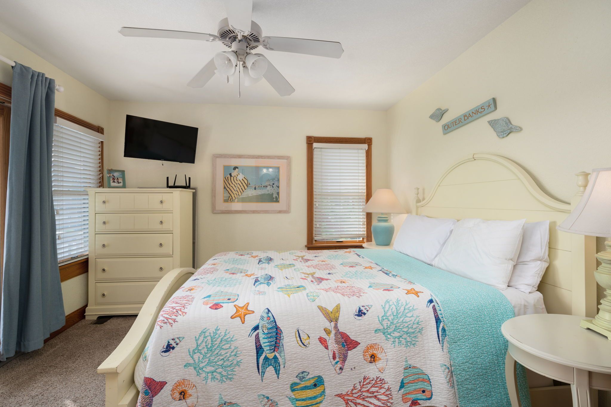 A bedroom with a bed, a dresser, a television, a ceiling fan, and a window with blinds.
