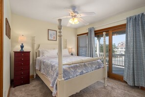 Un dormitorio con cama con dosel, ventilador de techo, cómoda y ventana con cortinas.