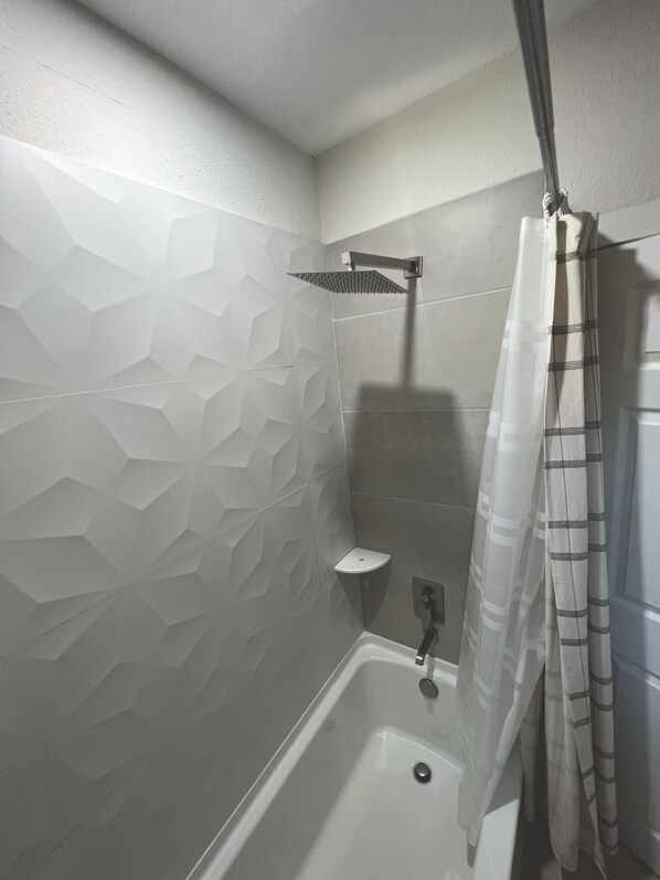 Un bagno moderno con una parete a motivi geometrici, una doccia con tenda a righe e una vasca da bagno bianca.