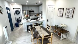 A compact kitchen with modern appliances, a dining area with a table and chairs, and a small seating area with a bench. - Luxury StayComfy at WinterHeaven (Winter Haven)