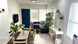 A modern living room with a dining area, a blue door, a grey sofa, and a large plant. - Luxury StayComfy at WinterHeaven (Winter Haven)