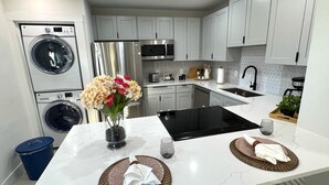 A modern kitchen with stainless steel appliances, a central island with a black induction cooktop, and a built-in oven. - Luxury StayComfy at WinterHeaven (Winter Haven)