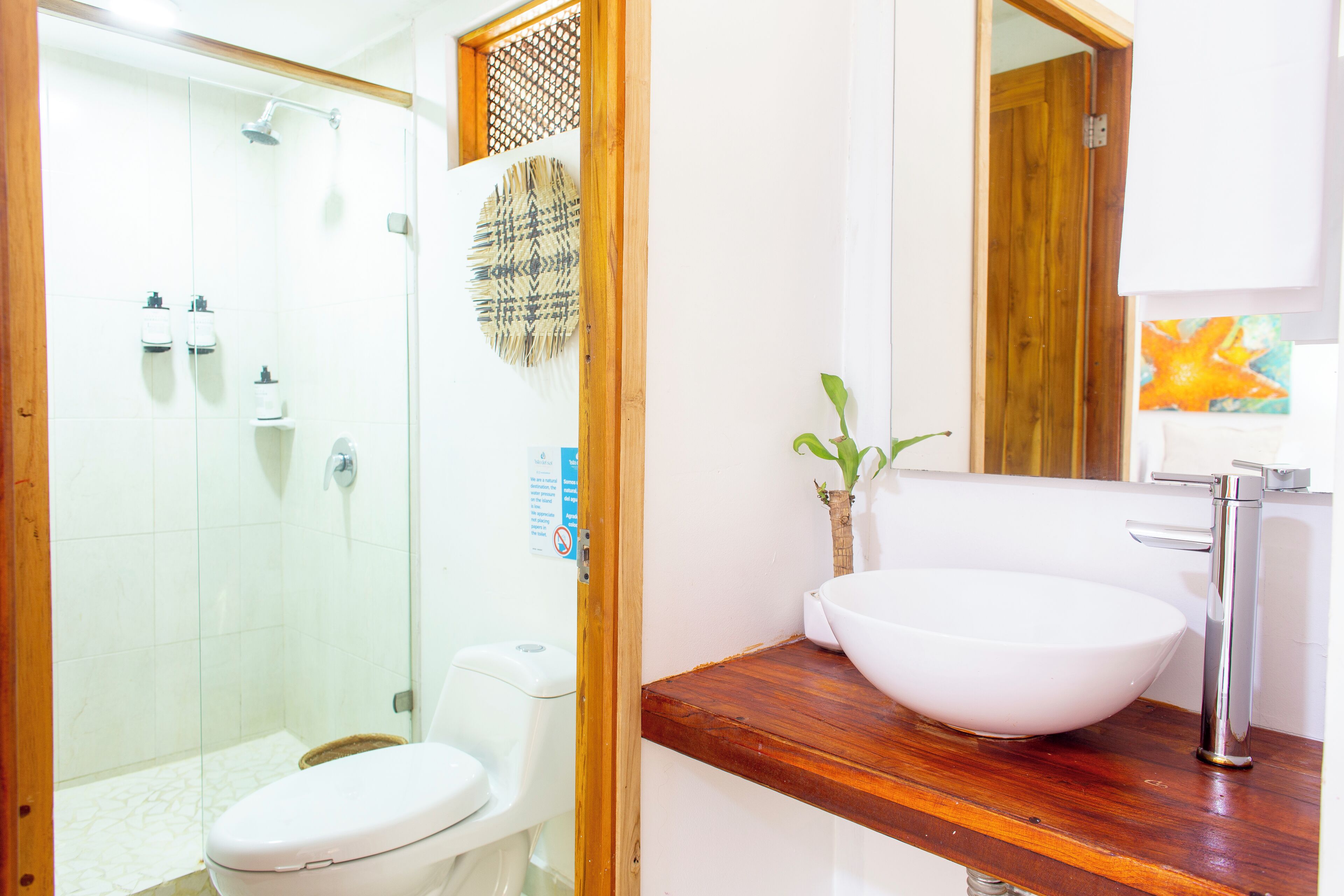 Un baño con cabina de ducha de vidrio, inodoro blanco, tocador de madera con lavamanos blanco y un espejo.