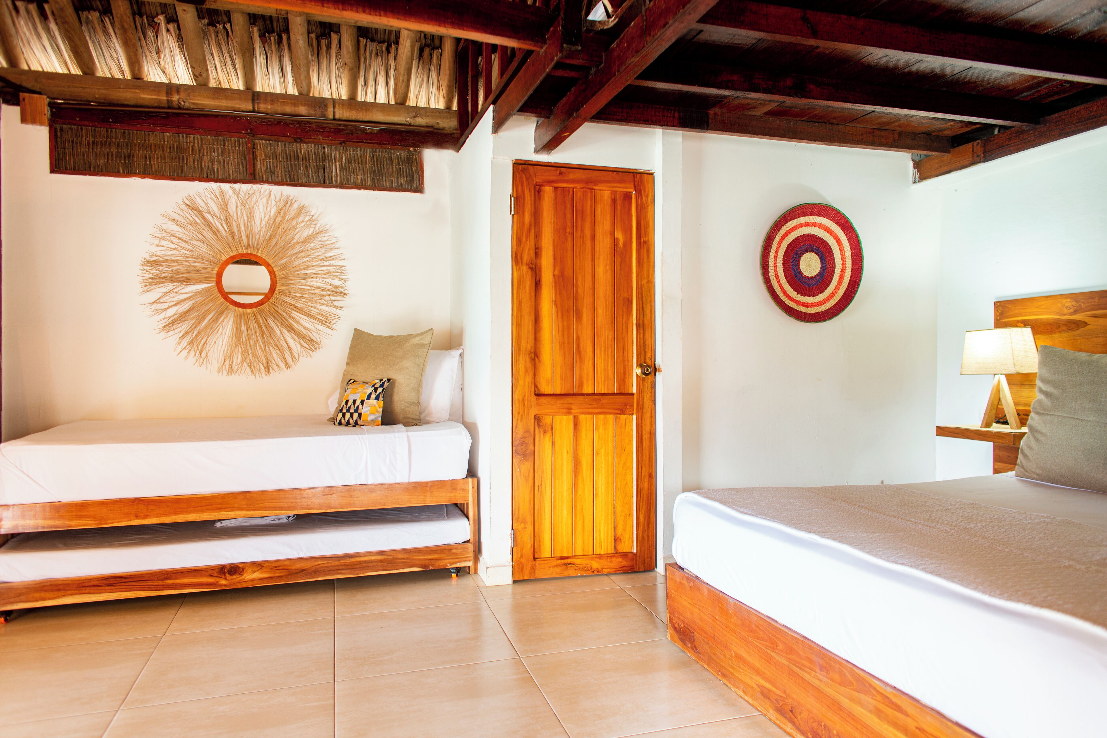 Una habitación con puerta de madera, una cama, un sofá, un adorno en la pared y una mesita de noche con lámpara.