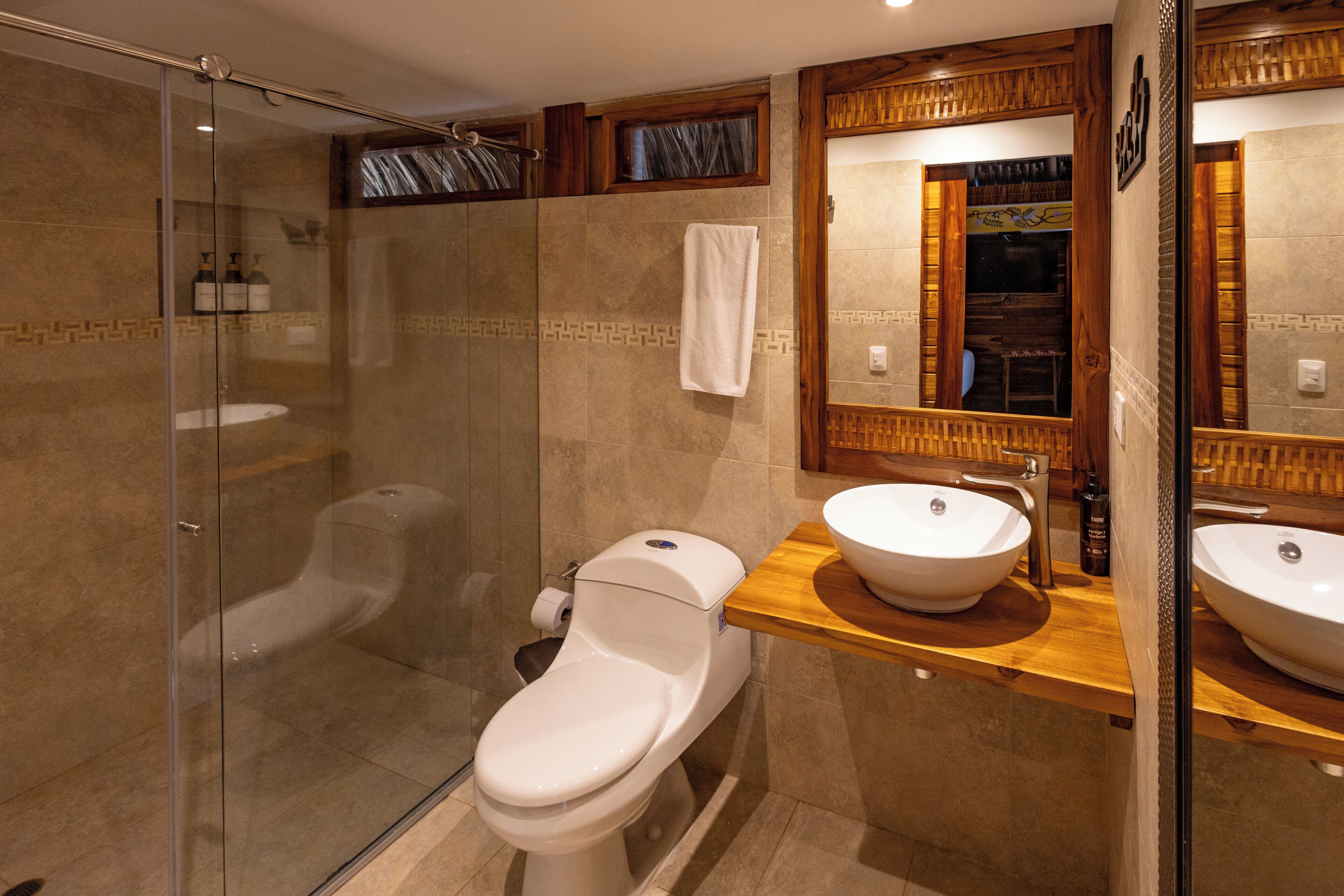 Een moderne badkamer met een glazen douchecabine, een wit toilet en een houten wastafelmeubel met een ruime wasbak.