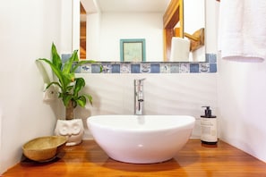 A bathroom with a white sink, a mirror, a potted plant, and a wooden countertop.