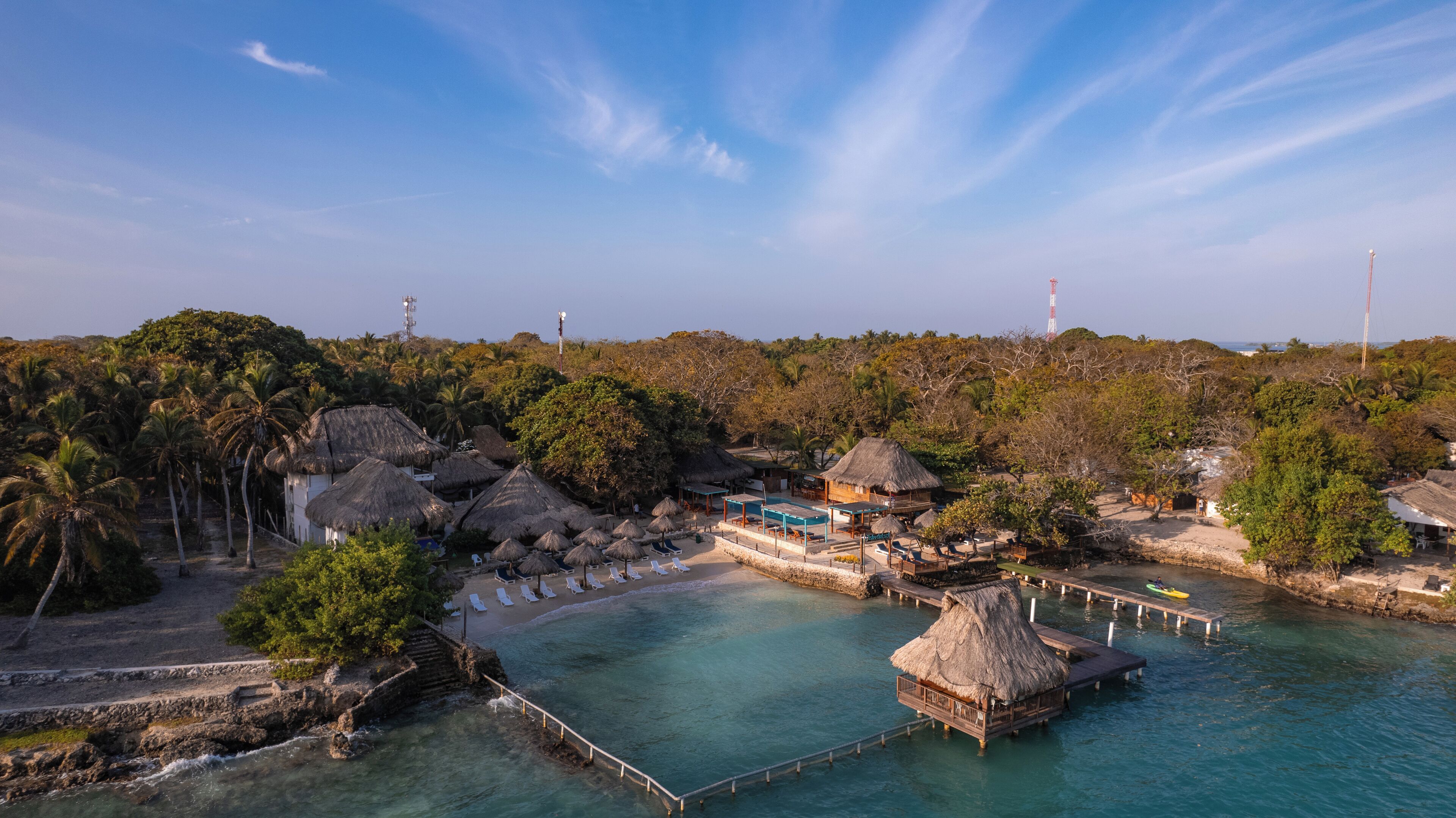 A tropical resort with thatched-roof huts, a swimming pool, and a pier extending into the water.