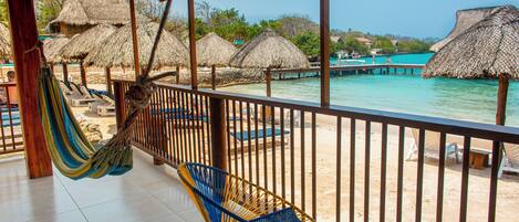 A beachside lounge with thatched umbrellas, a hammock, and lounge chairs.