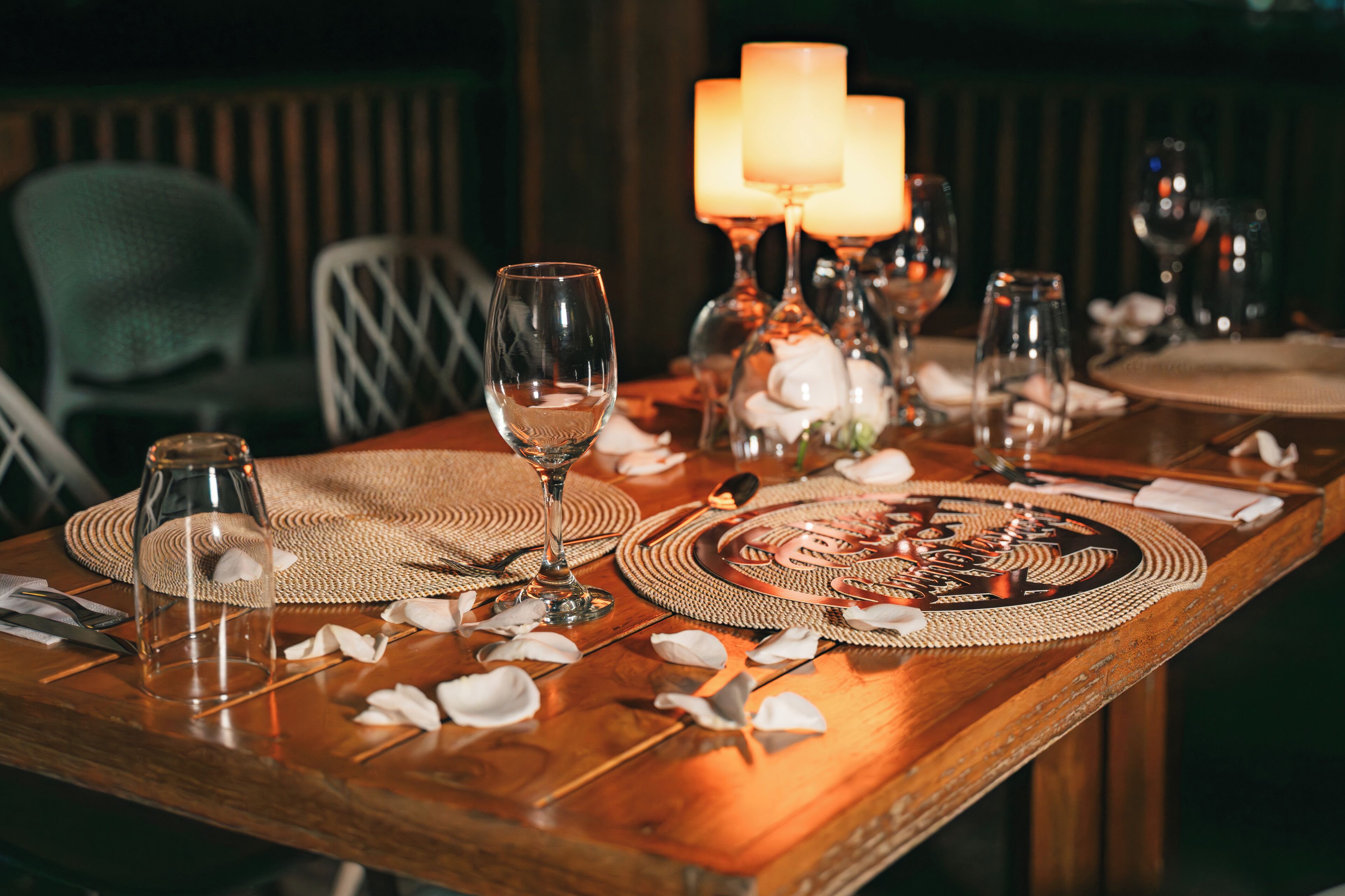 A dining table set with glassware, candles, and a placemat with a floral design.