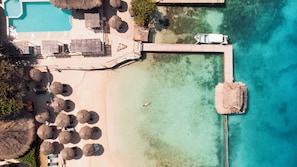 An aerial view of a beach resort with a swimming pool, umbrellas, lounge chairs, and a pier extending into the water. - Hotel Isla del Sol (Rosario Islands)