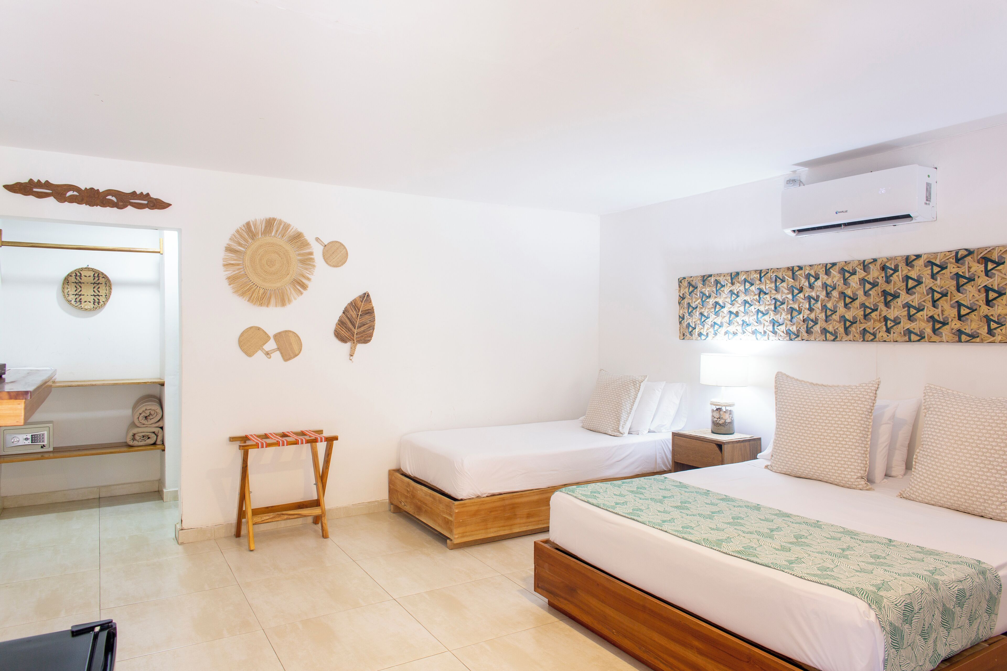 A bedroom with two single beds, a wooden side table, a wall-mounted air conditioner, and decorative wall art.