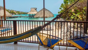 A beach view from a covered area with a hammock, chairs, and thatched umbrellas. - Hotel Isla del Sol  (Rosario Islands)
