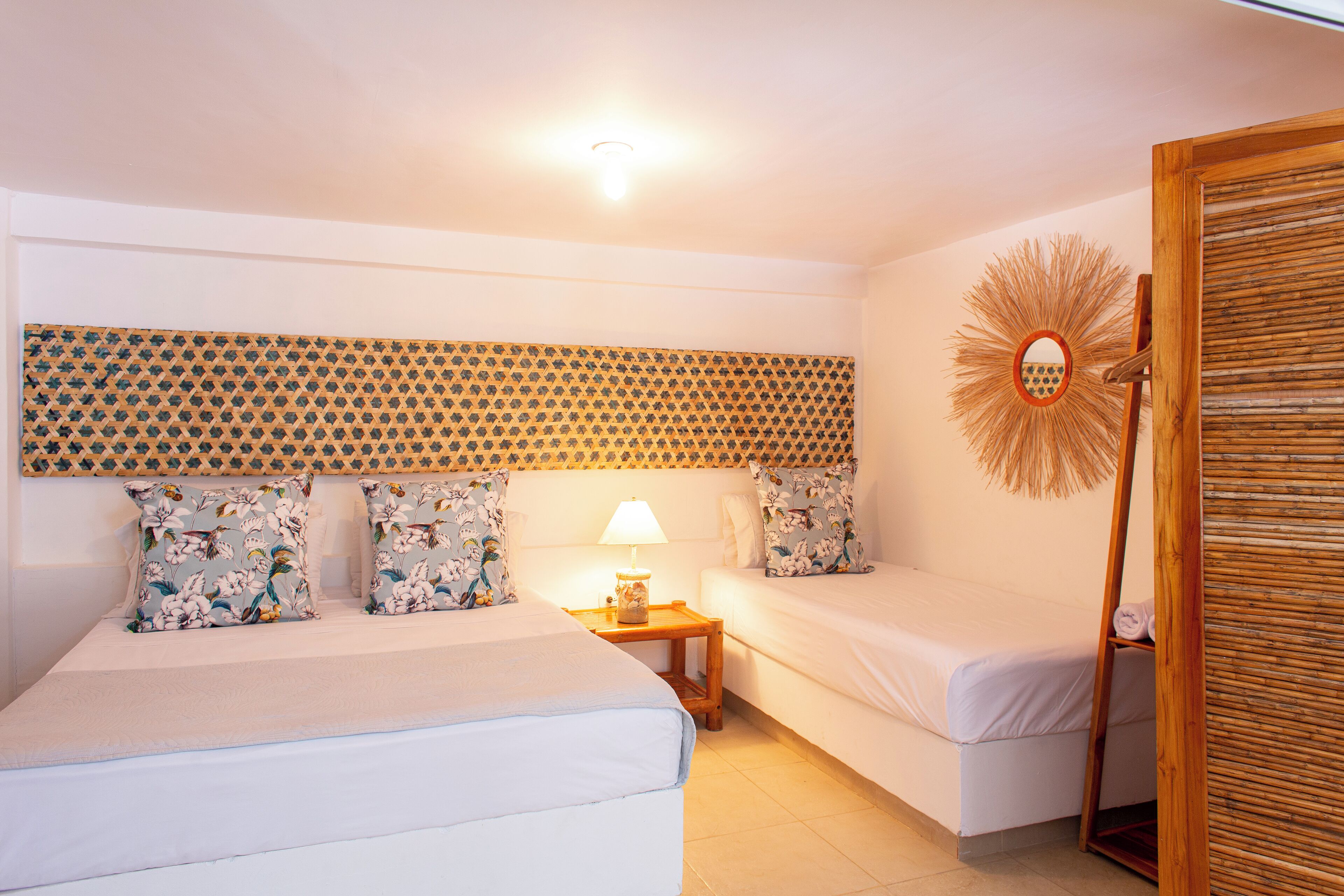 A hotel room with two beds, a wooden headboard, a wall-mounted mirror, and a small table with a lamp.