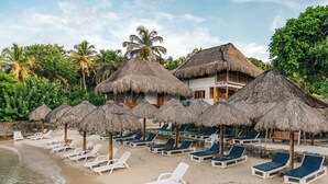 A beach resort with thatched-roof structures, lounge chairs, and a view of the ocean. - Hotel Isla del Sol  (Rosario Islands)