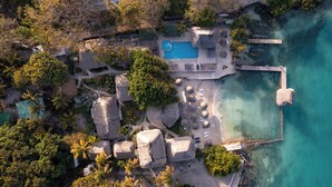 An aerial view of a resort with a swimming pool, thatched-roof structures, and a pier extending into a clear blue lagoon. - Hotel Isla del Sol  (Rosario Islands)
