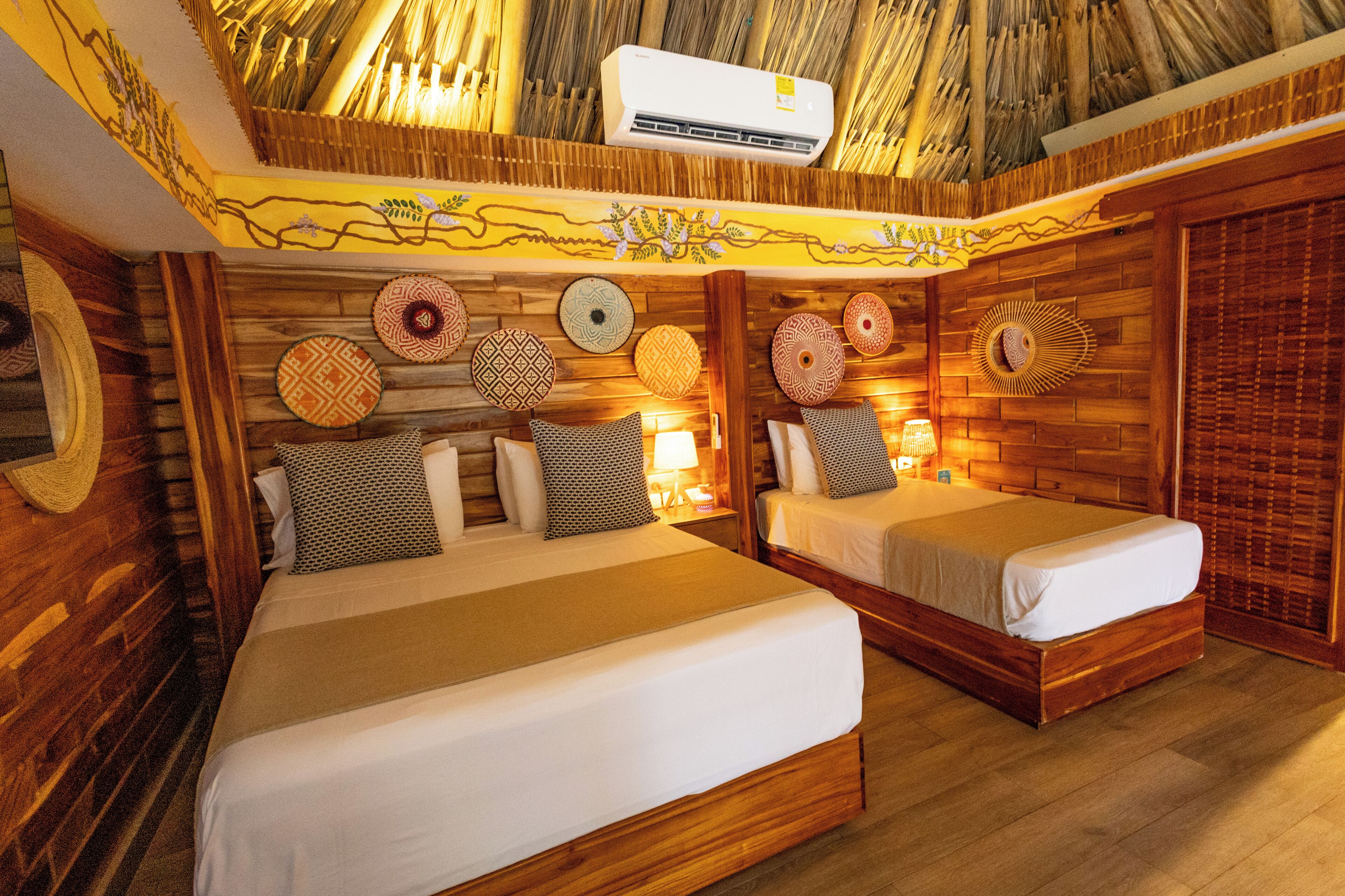 A room with two beds, wooden walls, and a thatched ceiling.