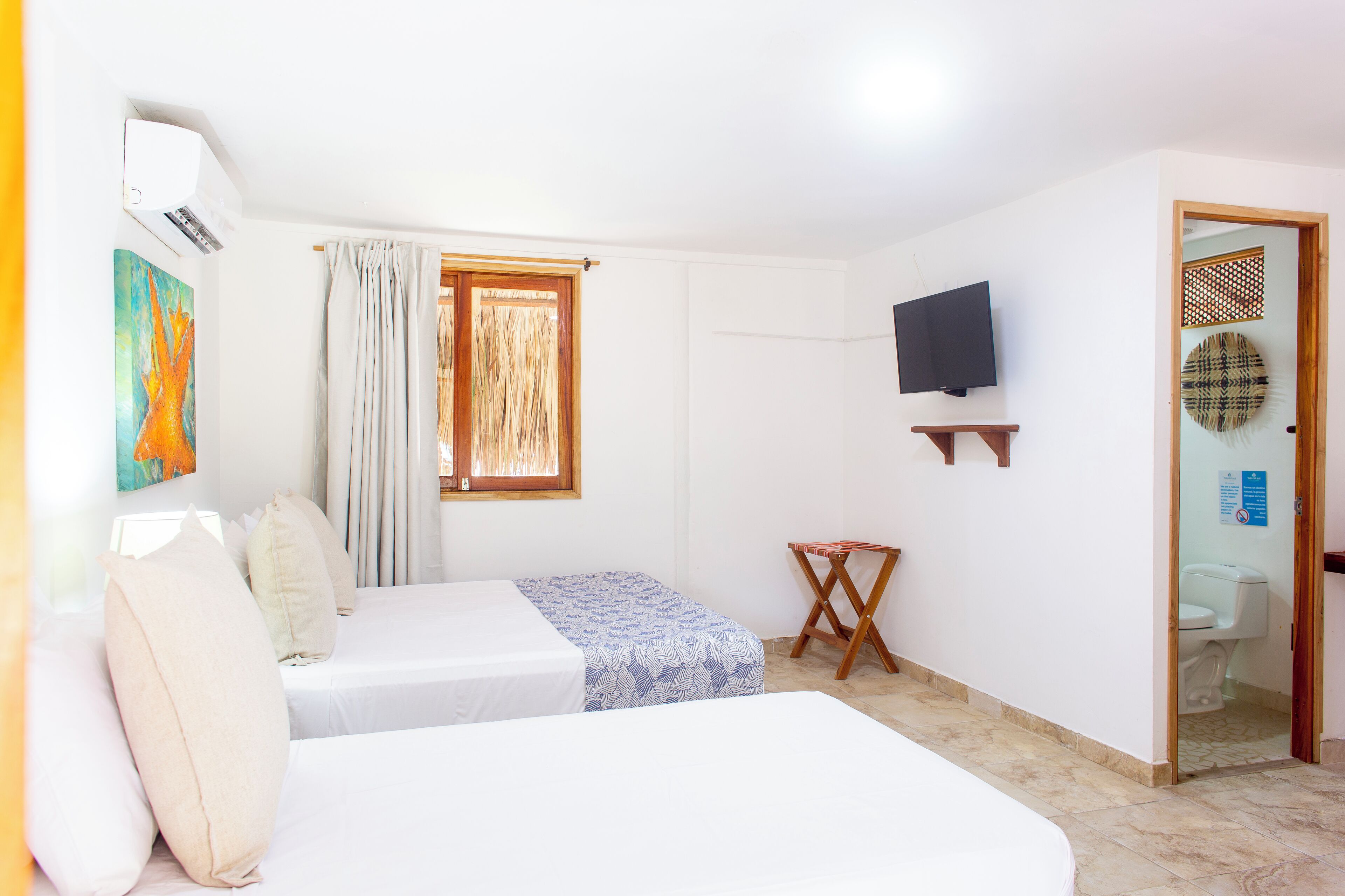 A hotel room with two beds, a TV, a window with curtains, and a small table.