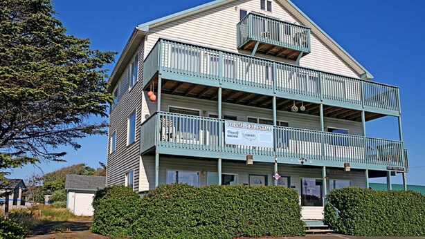 A two-story building with a balcony on the second floor, a sign for Coastal Real Estate, and a parking lot in front.
