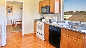 A modern kitchen with wooden cabinets, a microwave, a stove, and a dishwasher. There is a dining table with chairs and a window with a view of houses.