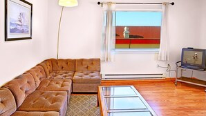 A living room with a sectional sofa, a glass coffee table, a television on a stand, and a window with curtains.