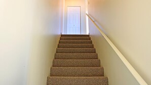 A carpeted staircase leading to a white door with a light fixture above.