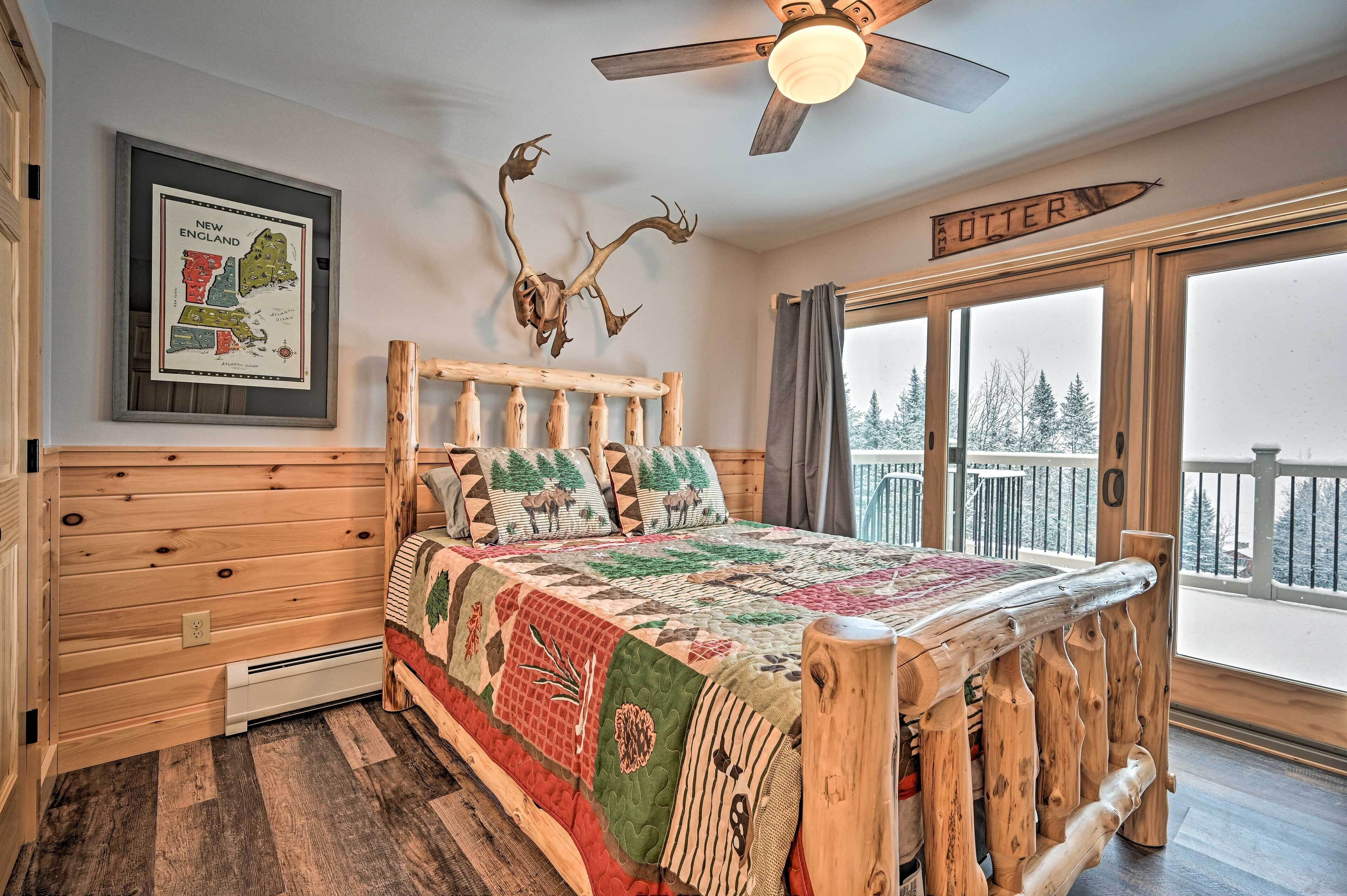 A wooden bedroom with a bed, a ceiling fan, a framed map, and a balcony with a view of snow-covered trees.