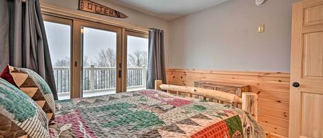 A cozy bedroom with a large bed, a wooden headboard, a ceiling fan, and a view of a snowy landscape through a sliding glass door.
