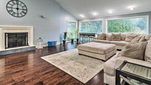 A spacious living room with a fireplace, a large window, and a modern clock on the wall.
