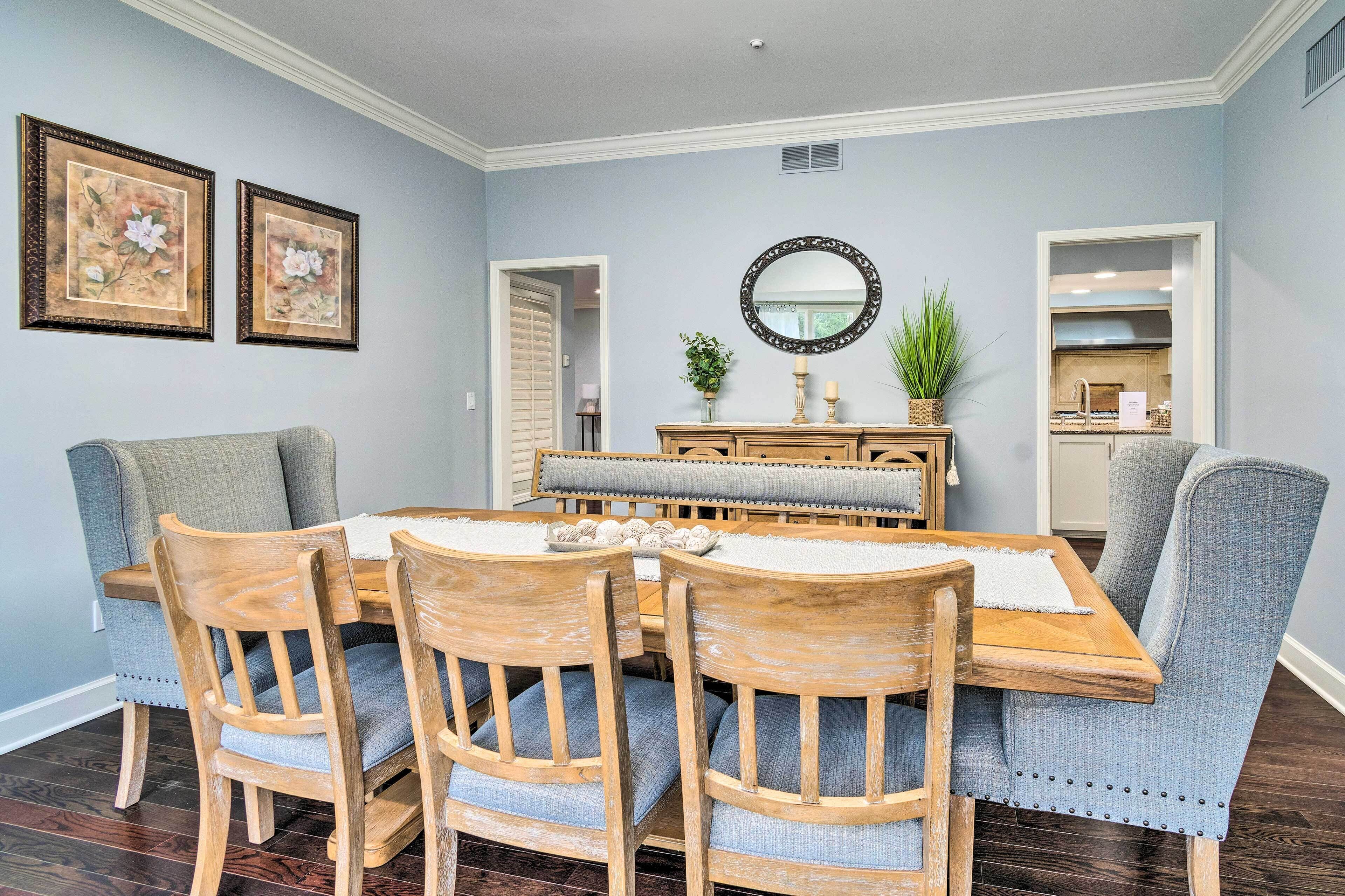 A dining room with a wooden table and four chairs, a mirror above the table, and two framed pictures on the wall.
