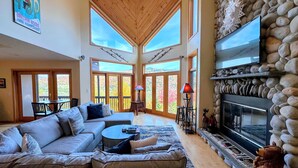 A spacious living room with a large sofa, a fireplace, and a stone wall.