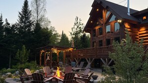A log cabin with a fire pit surrounded by Adirondack chairs, a deck, and a wooden deck railing. - WM dream home in National Forest; AC, swimspa, beach, massage chair, 2 min from ski area! (Bretton Woods)