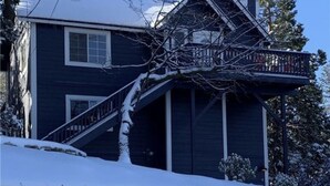 Une maison à deux étages, dont le toit est recouvert de neige et qui possède une terrasse en bois.