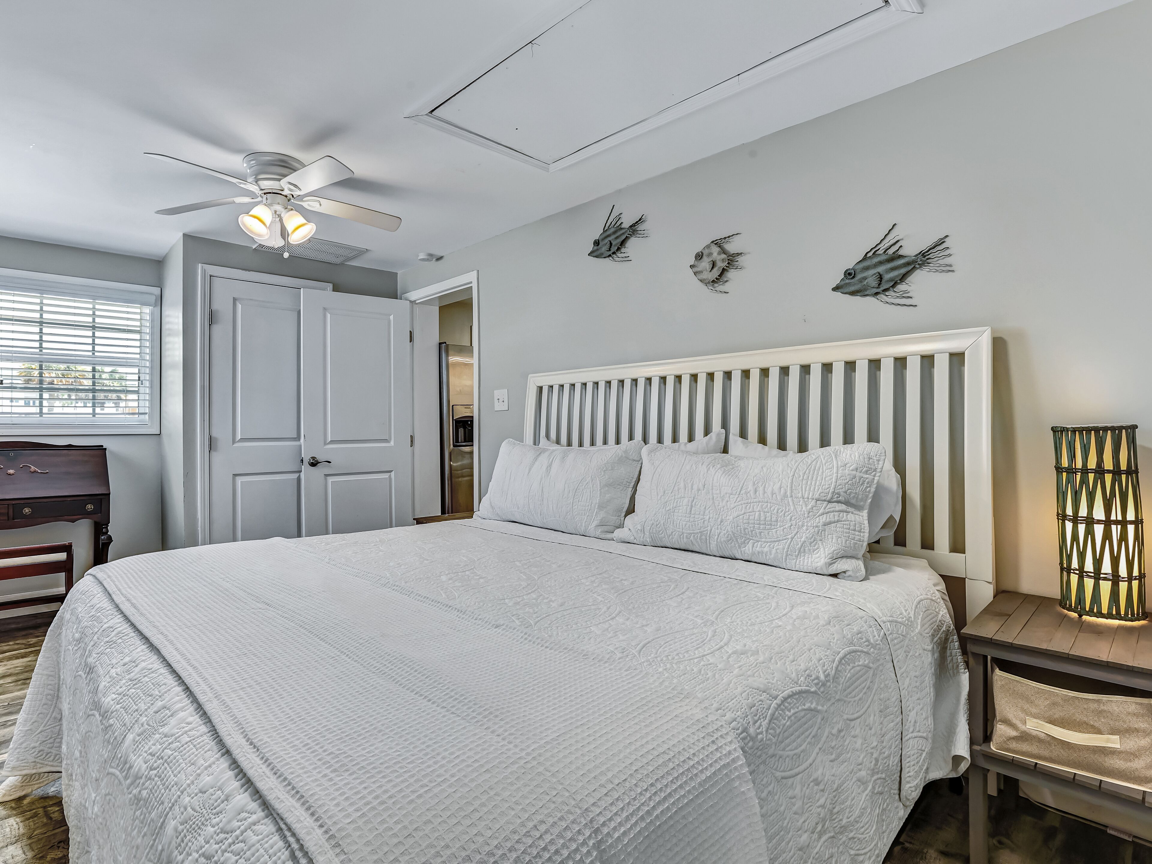 Une chambre à coucher comprenant un lit, un ventilateur de plafond, une commode et une table de chevet avec une lampe.