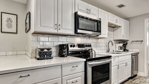 A modern kitchen with white cabinetry, a stainless steel range, a microwave, a coffee maker, and a toaster.
