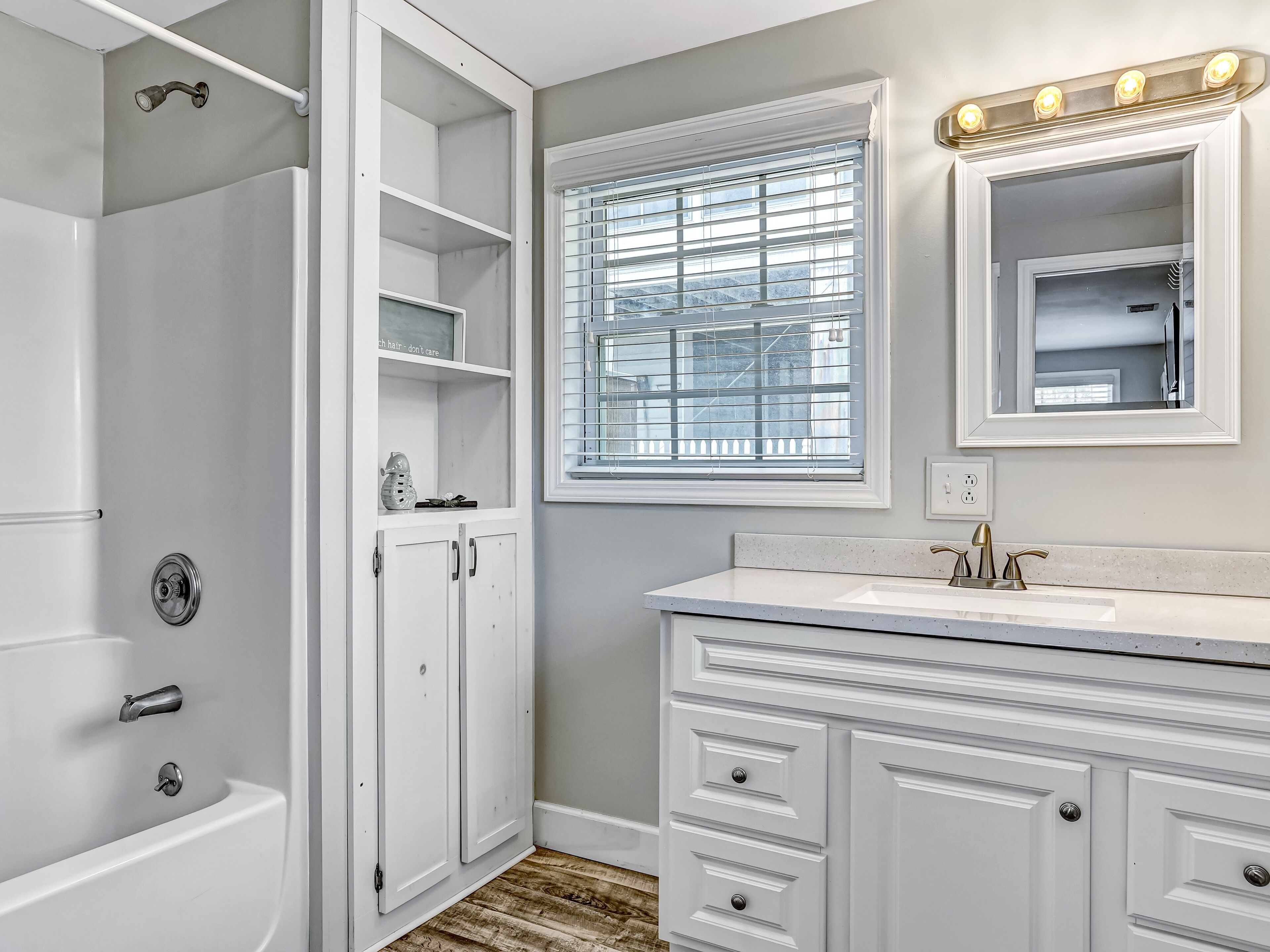 A bathroom with a walk-in shower, a vanity with a sink, and a window with blinds.