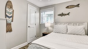 A bedroom with a bed, a door, a window with blinds, a ceiling fan, and wall art.
