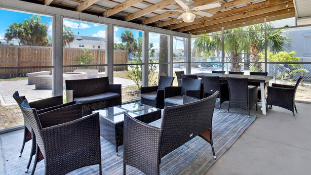 An outdoor patio with wicker furniture, a glass-top table, and a ceiling fan.