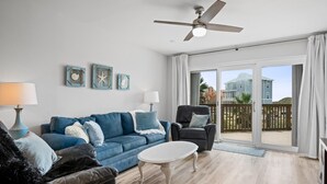 Ein Wohnzimmer mit einem blauen Sofa, einem weißen Couchtisch, einem schwarzen Sessel und einem Deckenventilator.
