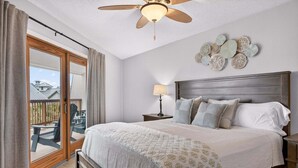 A bedroom with a bed, a ceiling fan, a nightstand, a lamp, and a view of the outside.