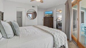 A bedroom with a bed, ceiling fan, TV, and a view of the outdoors.