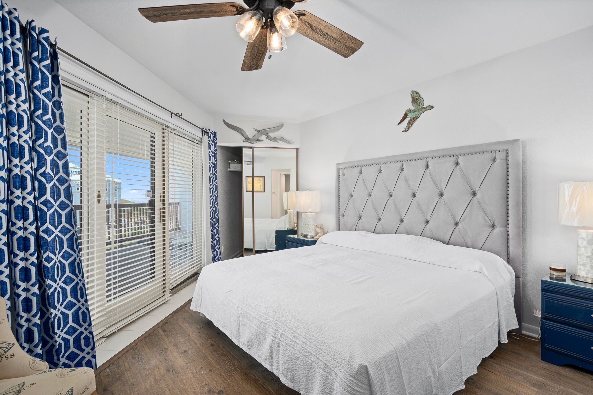 Ein Schlafzimmer mit einem großen Bett, einem Deckenventilator, einem Nachttisch und Blick ins Freie durch das Fenster.