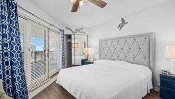 Ein Schlafzimmer mit einem großen Bett, einem Deckenventilator, einem Nachttisch und Blick ins Freie durch das Fenster.