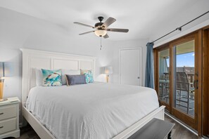 A bedroom with a bed, bedside lamps, a ceiling fan, and a sliding glass door to a balcony.