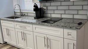 A modern kitchen with white cabinetry, a granite countertop, a built-in microwave, and a coffee maker. - Crystal Sands Apartments  (Ocean City)