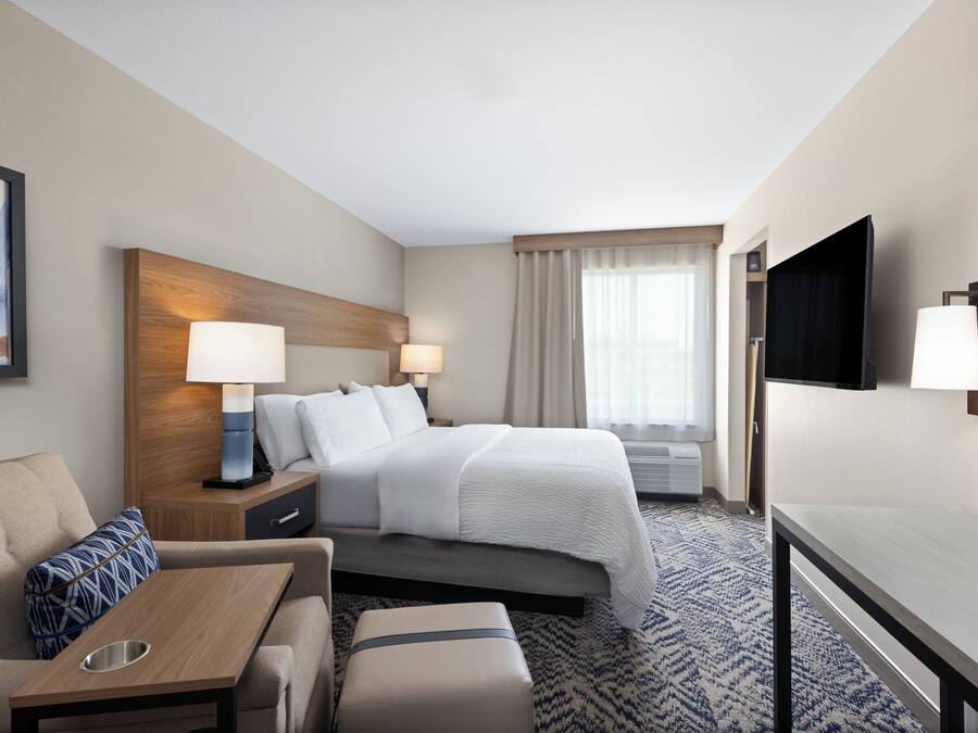 Een hotelkamer met een bed, nachtkastjes, een televisie, een bank en een kamerbreed tapijt met een patroon.
